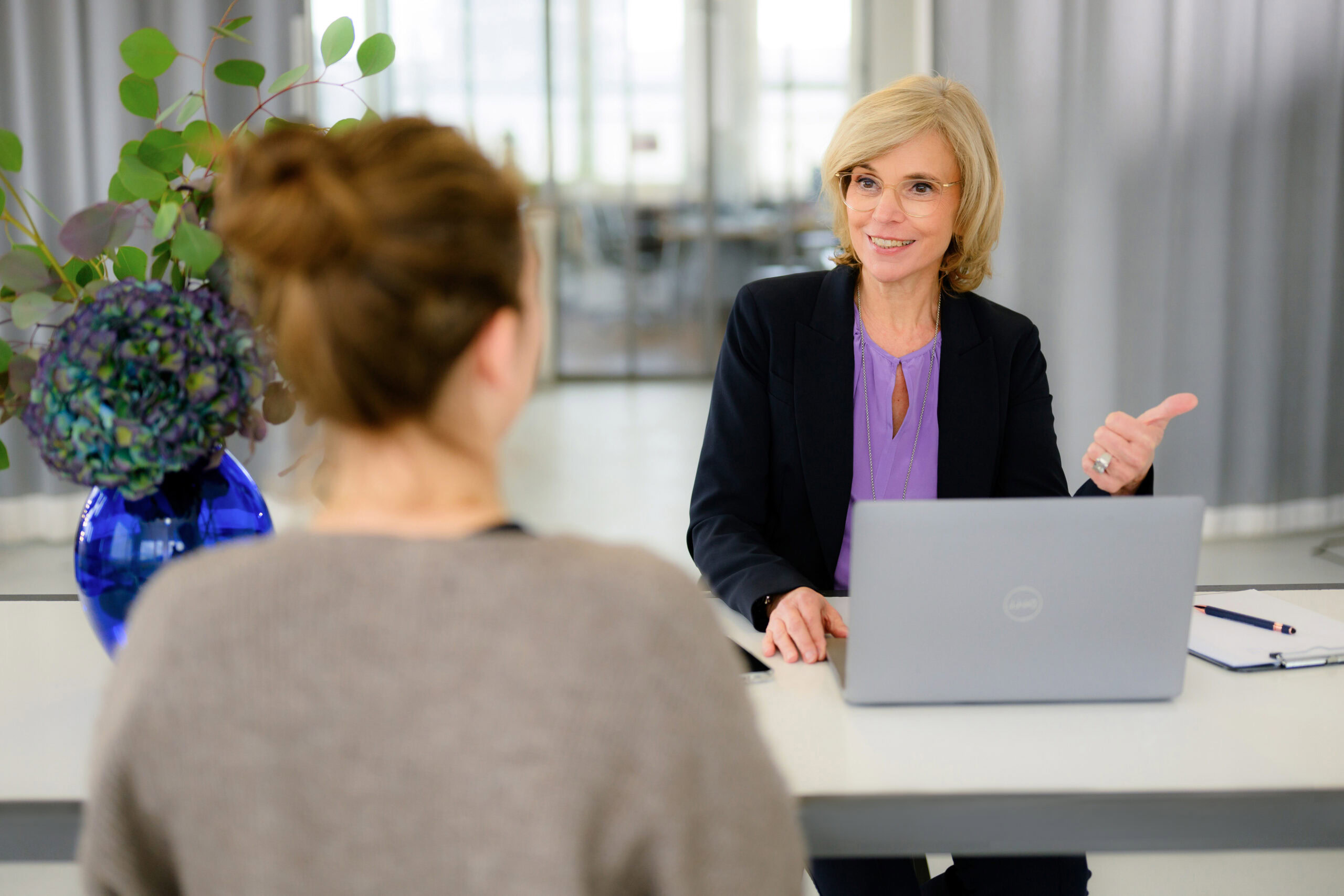 Verena Schiffer, Personalvermittlung München im Gespräch, sitzend am Schreibtisch vor aufgeklappten Laptop, ihr gegenüber sitzt eine Bewerberin